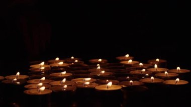 Arka planda bir el ile karanlık bir yüzeye dizilmiş, yanan mum. Tasarım ve prin için hatıra, anıt ve ruhani ritüel kavramı.