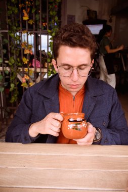 Beyaz İspanyol adam mavi ve turuncu giyinmiş geleneksel Meksika kil bardağından kahve içiyor.