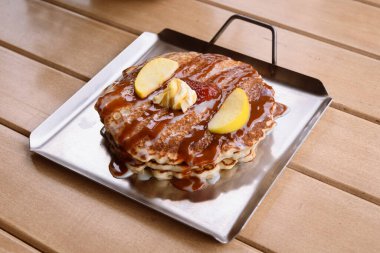 Geleneksel bir Amerikan kahvaltısı olan akçaağaç şurubu, tereyağı ve meyveli krep, ahşap bir masada metal bir tabakta servis edilir.