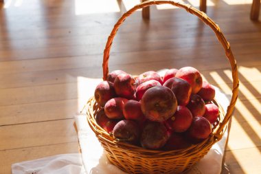Tahta zeminde kırmızı elmalarla örülmüş sepet.