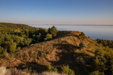 Etrafı Lush Trees, Grass ve Rocky Cliffs ile çevrili bir tepeden Serene Waterbody 'nin Hava Görüntüsü - Güzel Doğa Manzarası