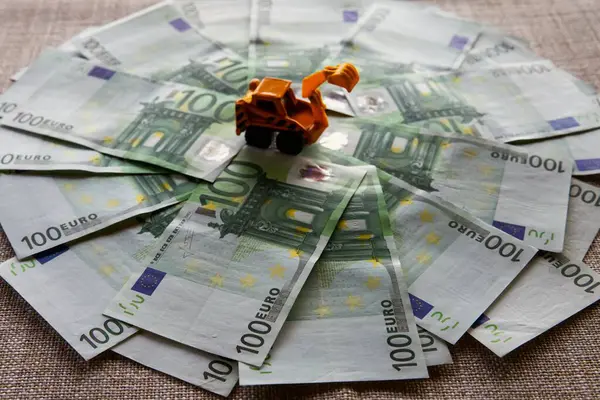 stock image     100 Euro Banknotes Fanned Out on a Table with a Construction Machine in the Background Symbolizing the Start of a New Building Project    