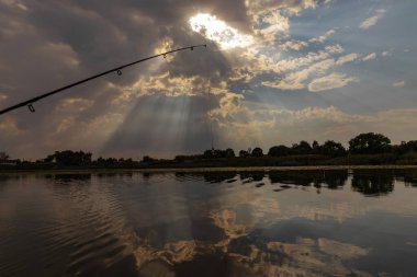 Landscape of Sunset Sky with a Fishing Rod in the Foreground, Active Recreation and Peaceful Atmosphere clipart