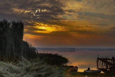 Gün batımında uzanan ahşap iskele, huzurlu doğa manzarası.