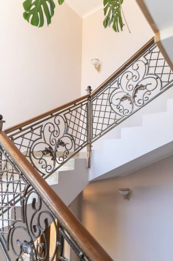 İçi demirden yapılmış merdiven ve aydınlık duvarlarla dolu. Şablonlu zarif metal parmaklıklar klasik bir tarz yaratır. Yeşil bitki yaprakları ve duvar lambaları konforlu ve dekoratif aksanlar ekler.