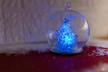 Glowing Christmas tree in a glass ornament with festive decorations in the background clipart