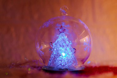 Cam bir süs içinde ışıldayan Noel ağacı ve arka planda şenlikli süsler.