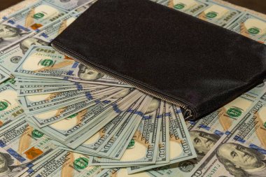 Black wallet and a fan of $100 dollar bills on a scattered money background clipart