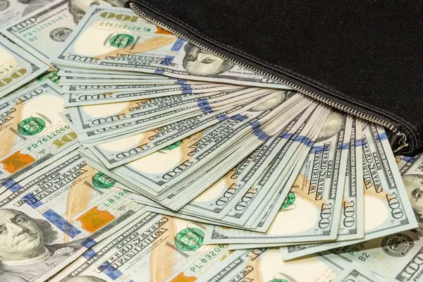 Siyah cüzdan ve dağınık bir para geçmişinde 100 dolarlık banknotlar.