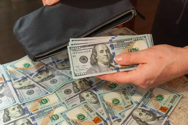 Kumaş arka planında 100 dolarlık banknotları tutan el.