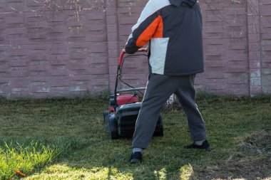 Arka bahçesinde çim biçme makinesi olan bir kişi.