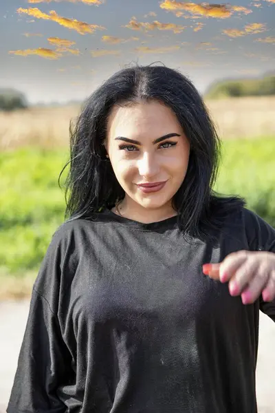 Güneşli bir günde siyah giysili kendinden emin genç bir kadının portresi doğal bir arka plana karşıdır.