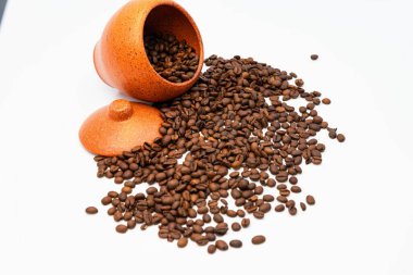 Scattered roasted coffee beans from a ceramic jar on a white background clipart