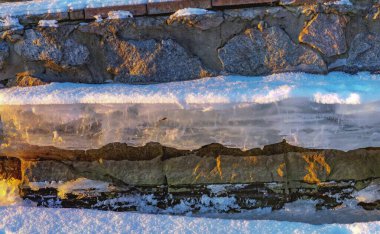 Thick ice block covered with snow on a stone wall on a winter day. clipart