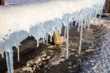 Buz saçaklarının kışın karla kaplı ahşap iskelede asılı olduğu yakın plan.