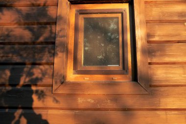 Sıcak güneş ışığı ve ağaç gölgelerinde penceresi olan ahşap bir ev duvarı.