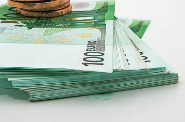 Beyaz bir zemin ve finansal konsept üzerinde çikolata euro bozukluklarla dolu 100 avroluk banknot yığını.