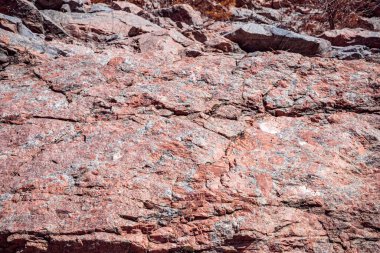 Doğal çatlaklar ve gölgeli pembe granit kaya dokusunun yakın çekimi, tasarım veya doğa temalı projeler için jeolojik arkaplan