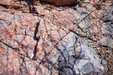 Doğal çatlaklar ve gölgeli pembe granit kaya dokusunun yakın çekimi, tasarım veya doğa temalı projeler için jeolojik arkaplan