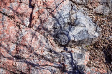 Doğal çatlaklar ve gölgeli pembe granit kaya dokusunun yakın çekimi, tasarım veya doğa temalı projeler için jeolojik arkaplan