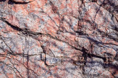 Doğal çatlaklar ve gölgeli pembe granit kaya dokusunun yakın çekimi, tasarım veya doğa temalı projeler için jeolojik arkaplan