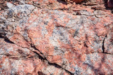 Doğal çatlaklar ve gölgeli pembe granit kaya dokusunun yakın çekimi, tasarım veya doğa temalı projeler için jeolojik arkaplan