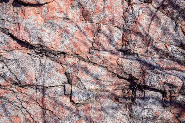 Doğal çatlaklar ve gölgeli pembe granit kaya dokusunun yakın çekimi, tasarım veya doğa temalı projeler için jeolojik arkaplan