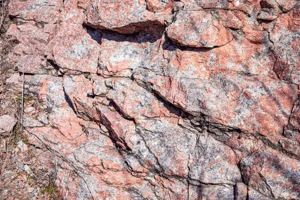Doğal çatlaklar ve gölgeli pembe granit kaya dokusunun yakın çekimi, tasarım veya doğa temalı projeler için jeolojik arkaplan