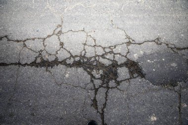 Kırık asfalt yol yüzeyinde geniş çatlaklar, kentsel grunge dokusu arka planı
