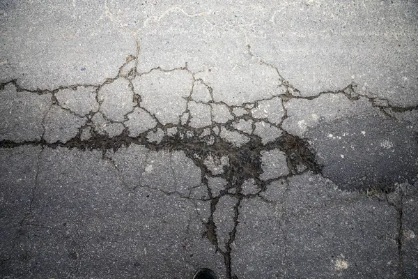 Kırık asfalt yol yüzeyinde geniş çatlaklar, kentsel grunge dokusu arka planı