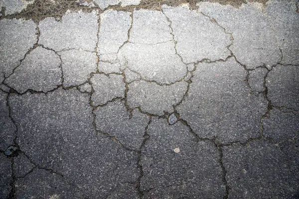 Kırık asfalt yol yüzeyinde geniş çatlaklar, kentsel grunge dokusu arka planı