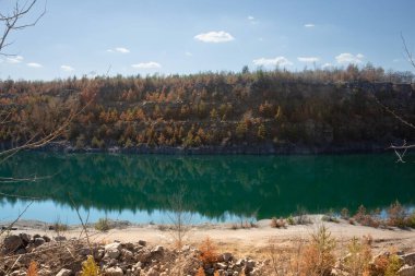 Kayalık uçurum ve ormanın manzarası taş ocağı gölünün turkuaz suyuna yansıyor.