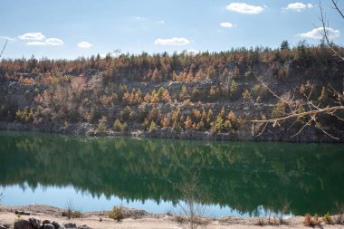 Kayalık uçurum ve ormanın manzarası taş ocağı gölünün turkuaz suyuna yansıyor.