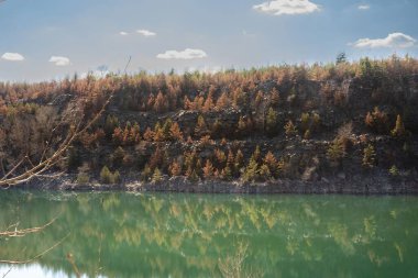 Kayalık uçurum ve ormanın manzarası taş ocağı gölünün turkuaz suyuna yansıyor.
