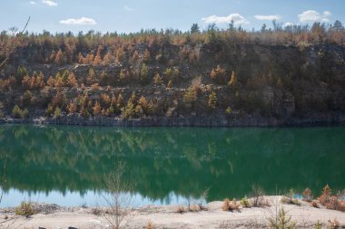 Kayalık uçurum ve ormanın manzarası taş ocağı gölünün turkuaz suyuna yansıyor.