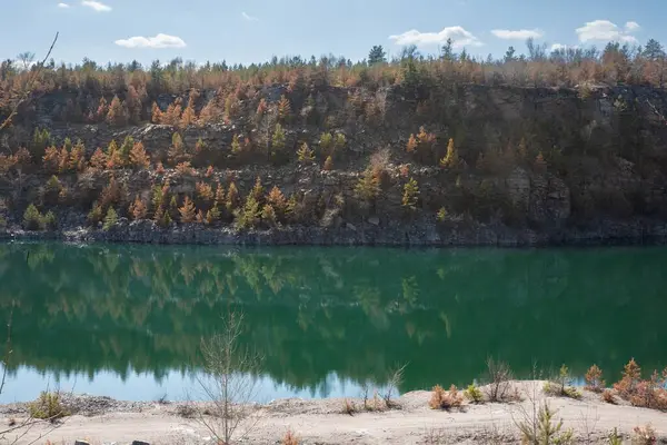 Kayalık uçurum ve ormanın manzarası taş ocağı gölünün turkuaz suyuna yansıyor.