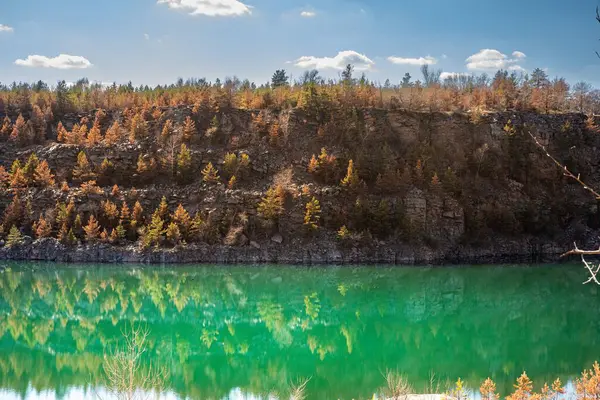 Kayalık uçurum ve ormanın manzarası taş ocağı gölünün turkuaz suyuna yansıyor.