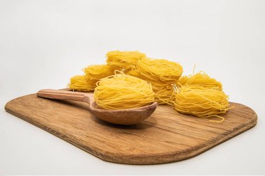 Beyaz arka planda izole edilmiş tahta bir kaşıkta kuru makarna yuvaları. Pişmemiş İtalyan spagettisi. Yakın plan..