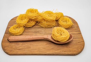 Beyaz arka planda izole edilmiş tahta bir kaşıkta kuru makarna yuvaları. Pişmemiş İtalyan spagettisi. Yakın plan..