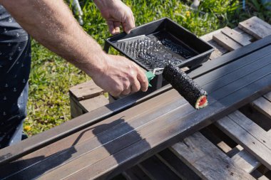 Güneşli bir günde, dışarıda paten fırçasıyla metal bir yapı boyamak, boyama sürecinin ve işçilerin ellerinin yakın çekimi.