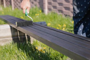 Güneşli bir günde, dışarıda paten fırçasıyla metal bir yapı boyamak, boyama sürecinin ve işçilerin ellerinin yakın çekimi.