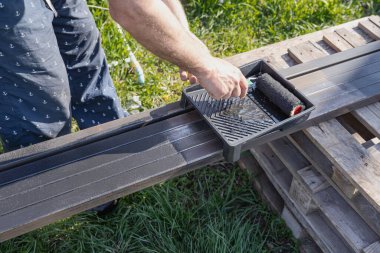 Güneşli bir günde, dışarıda paten fırçasıyla metal bir yapı boyamak, boyama sürecinin ve işçilerin ellerinin yakın çekimi.
