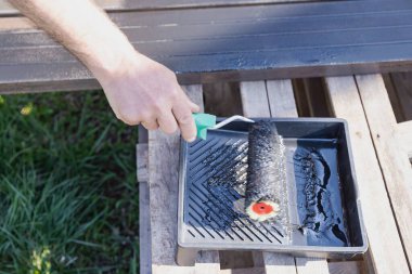Güneşli bir günde, dışarıda paten fırçasıyla metal bir yapı boyamak, boyama sürecinin ve işçilerin ellerinin yakın çekimi.