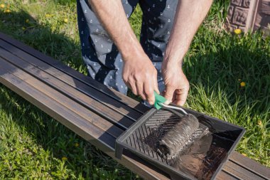 Güneşli bir günde, dışarıda paten fırçasıyla metal bir yapı boyamak, boyama sürecinin ve işçilerin ellerinin yakın çekimi.