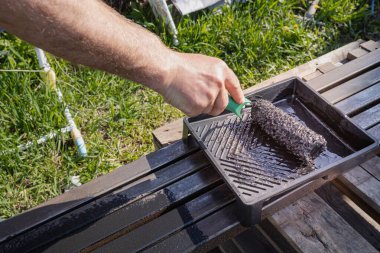 Güneşli bir günde, dışarıda paten fırçasıyla metal bir yapı boyamak, boyama sürecinin ve işçilerin ellerinin yakın çekimi.