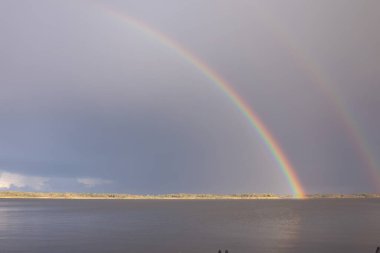 Yağmurdan sonra dramatik gökyüzü altında, sakin göl üzerinde çift gökkuşağı, doğal arka plan