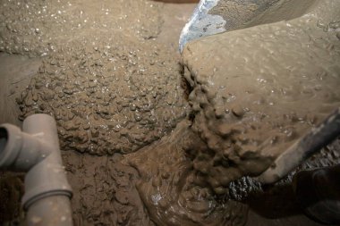 İnşaat alanındaki plastik borunun yakınındaki el arabasından taze beton dökülüyor.