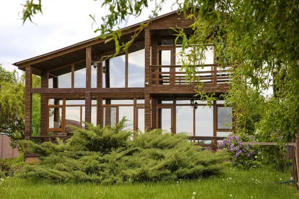 Eko ahşap ev, büyük cam pencereler ve kırsal alanda bahar leylak çalıları.