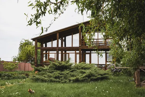 Eko ahşap ev, büyük cam pencereler ve kırsal alanda bahar leylak çalıları.
