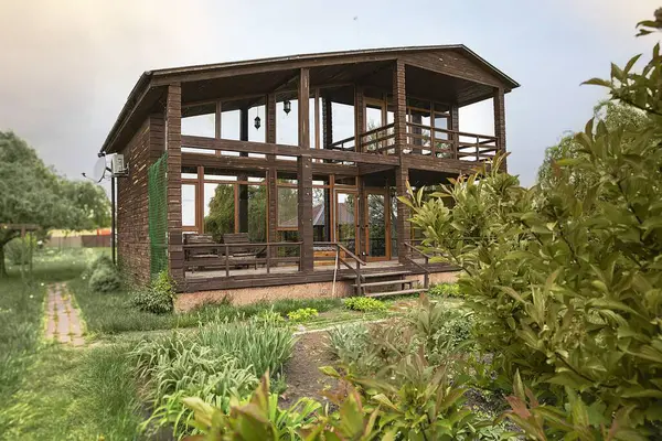 Eko ahşap ev, büyük cam pencereler ve kırsal alanda bahar leylak çalıları.